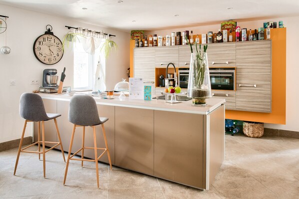 A modern kitchen with a central island, bar stools, a clock, and a variety of kitchen appliances and storage cabinets.