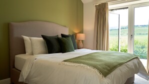 A bedroom with a bed, pillows, a lamp, and a view through an open door.