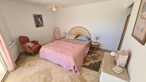 Quarto com cama, cadeira, mesa pequena, luminária, pôster na parede e espelho.