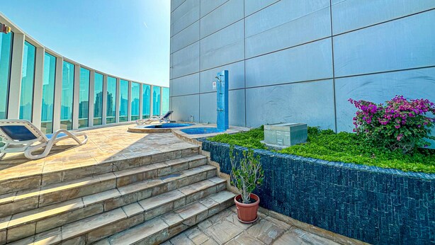 A modern building with a large glass facade, a pool area with lounge chairs, and a staircase leading to the entrance. - HiGuests - Madison Residency (Dubai)