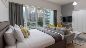 A modern hotel room with a large bed, a sofa, a TV, and a balcony with a view of the city. - HiGuests - Madison Residency (Dubai)