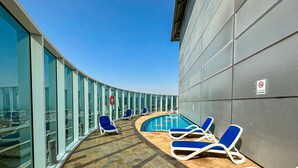 A sun deck with a pool, lounge chairs, and a view of the city. - HiGuests - Madison Residency (Dubai)