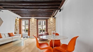 A modern living room with a glass coffee table, orange chairs, a white sofa, and a stone wall. - Lucius, 1BR/1BA, 2 people (París)