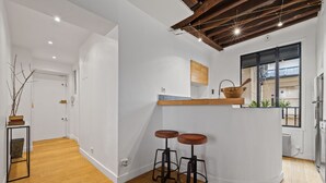 A modern kitchen with wooden stools, a hanging pot rack, and a large window. - Lucius, 1BR/1BA, 2 people (París)