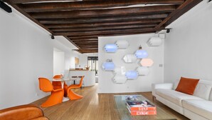 A modern interior with a wooden ceiling, a white sofa, orange chairs, and a glass coffee table with books. - Lucius, 1BR/1BA, 2 people (París)