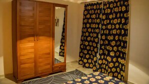 A bedroom with a wooden wardrobe, a bed with a floral bedspread, and a curtain with a sunflower pattern. - Jamila basement apartment (New Cairo)