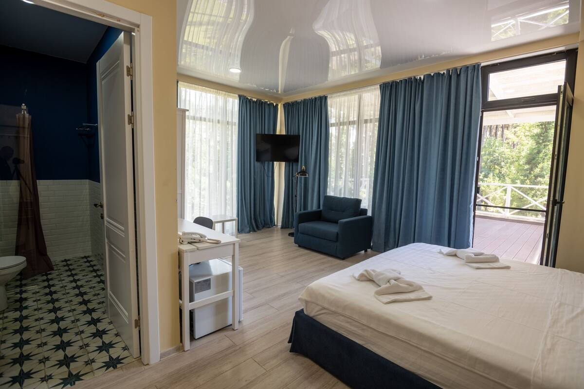 Une chambre d’hôtel avec un lit, un bureau, une chaise, une télévision et un balcon avec des rideaux.
