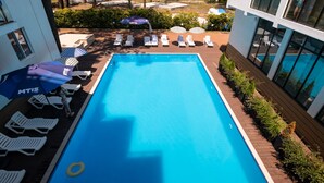 A swimming pool with lounge chairs and umbrellas, surrounded by a landscaped garden and a building with large windows.