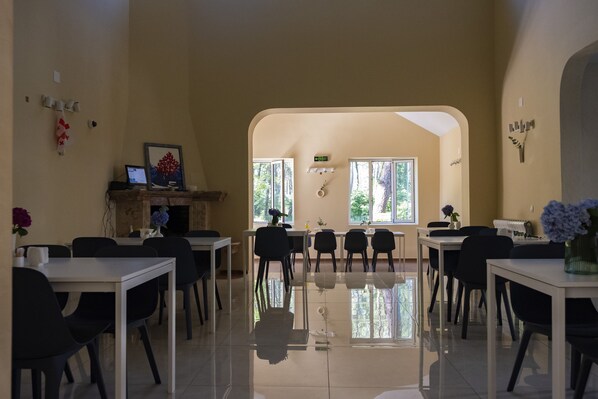 A spacious dining area with multiple tables and chairs, a fireplace, and large windows allowing natural light.