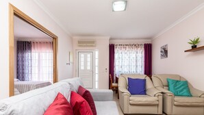 A living room with a grey sofa, red and blue cushions, a beige armchair, and a small table with a plant. - 4 bedroom villa in condominium with swimming pool by AlgarveManta (9V4) (Manta Rota)