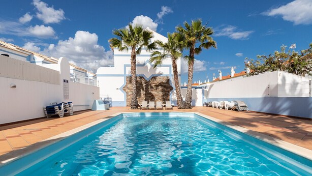 A swimming pool with clear blue water, surrounded by white walls and palm trees. - 4 bedroom villa in condominium with swimming pool by AlgarveManta (9V4) (Manta Rota)