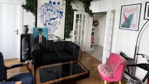 A living room with a black leather sofa, a pink chair, a glass coffee table, and a bicycle. - Artist's'apartment Paris 18 (Paris)