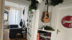 Una habitación con piso de madera, un sofá negro, una guitarra, un zapatero y una puerta con un adorno circular rojo.