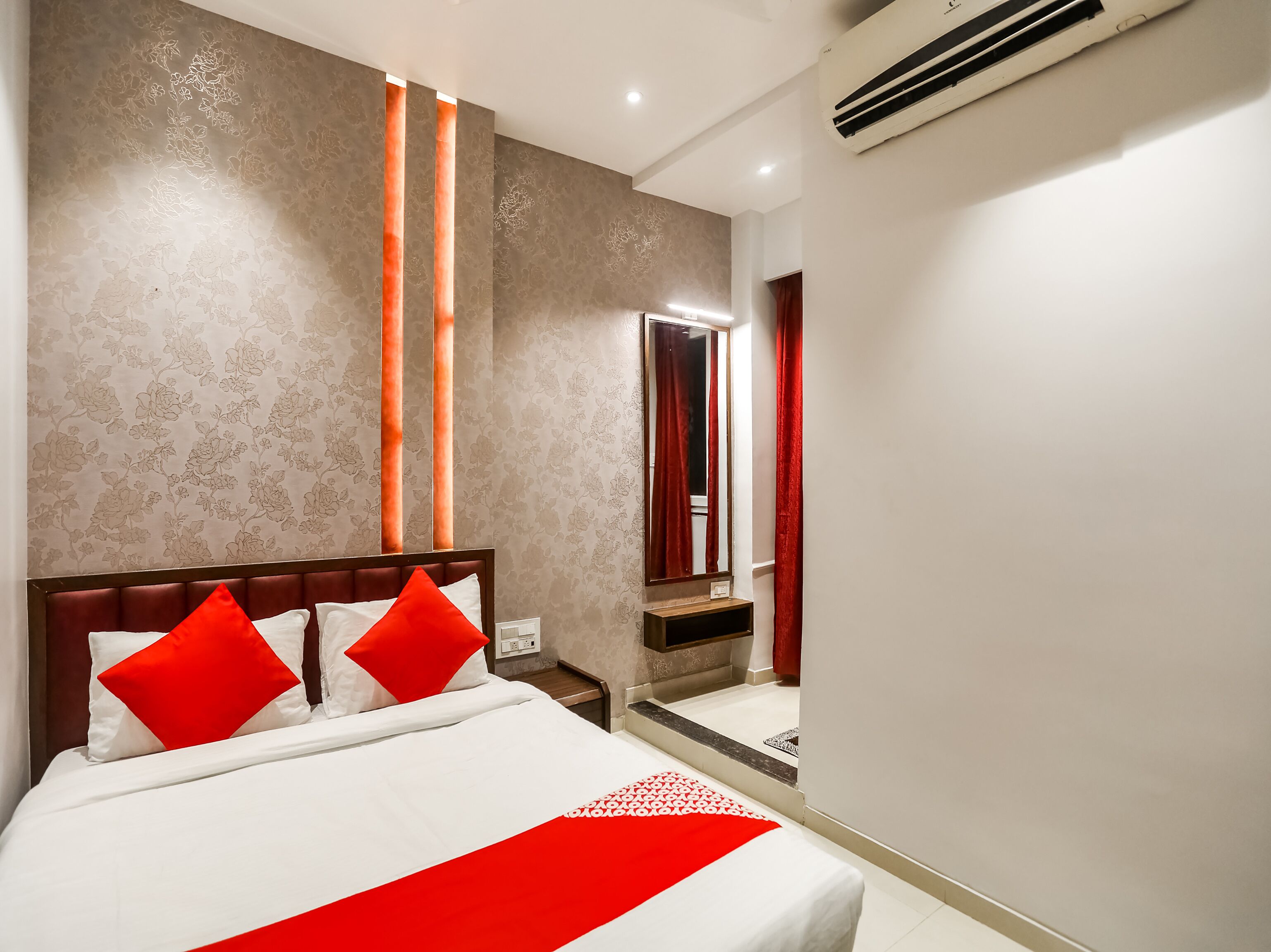 A hotel room with a bed, a nightstand, a mirror, and a red curtain.
