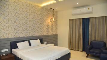 A bedroom with a large bed, a nightstand, a chair, a ceiling fan, and an air conditioning unit.