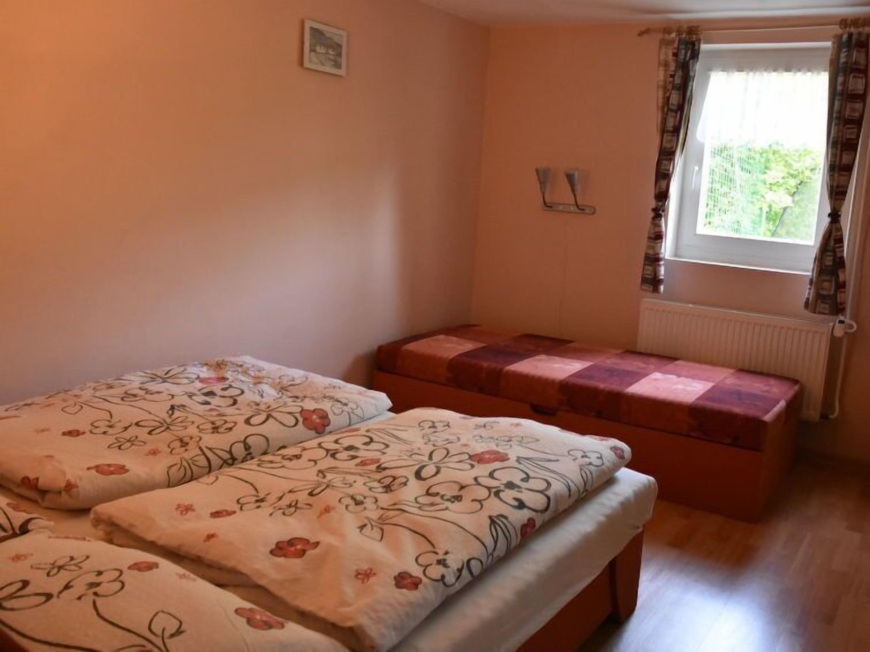 A bedroom with two beds, a window with curtains, a radiator, and a small picture on the wall.