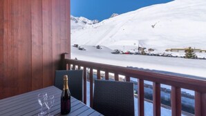 Eine Holzterrasse mit Tisch und Stühlen, mit Blick auf einen verschneiten Berg mit Skipisten und Gebäuden.