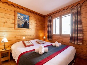 A wooden cabin room with a bed, two bedside lamps, a window with curtains, and a painting on the wall. - Ecrin des Neiges (Val Claret) by Interhome (Tignes)