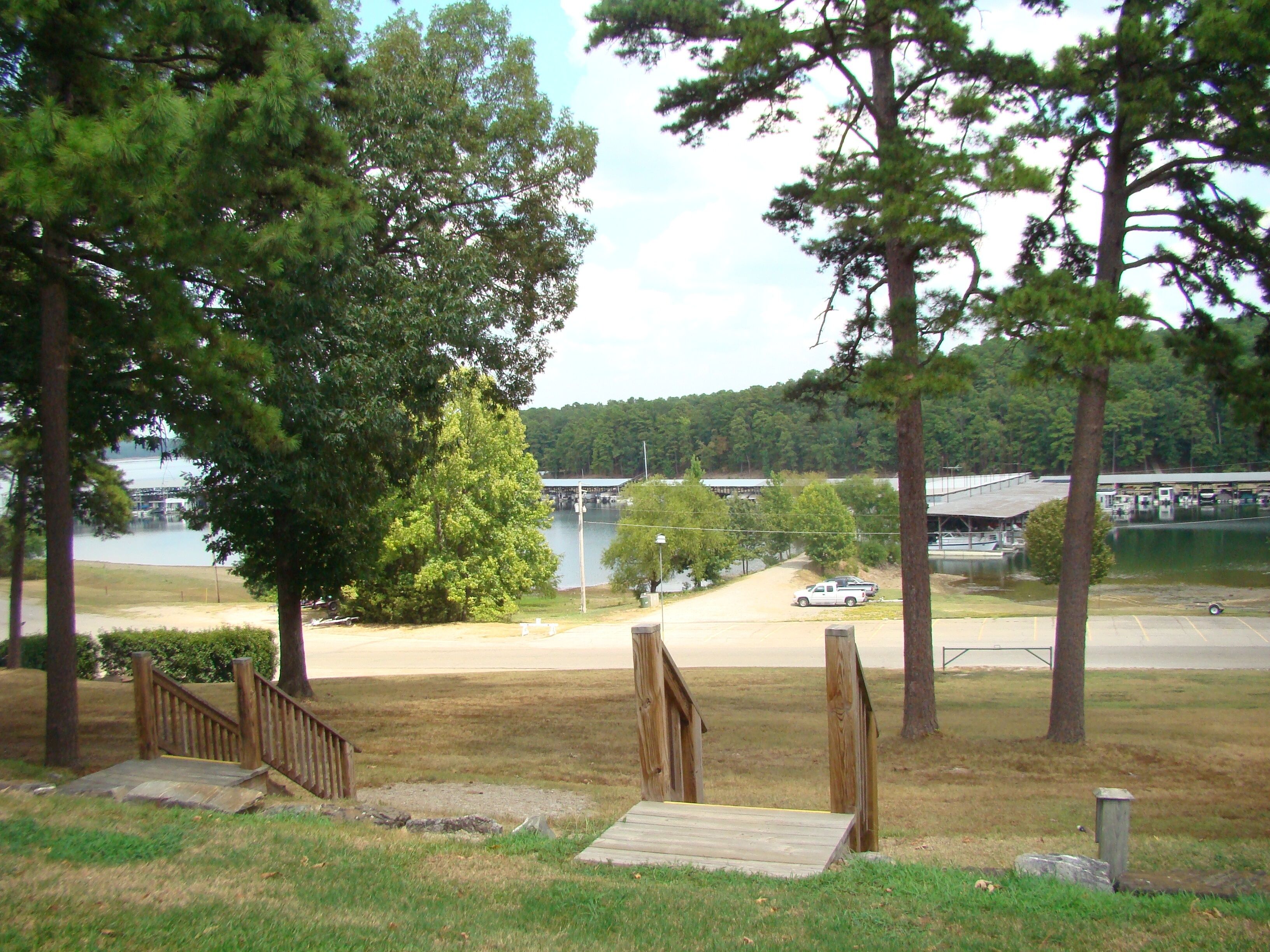 A view of a parking area with a bridge in the background, surrounded by trees and a body of water.