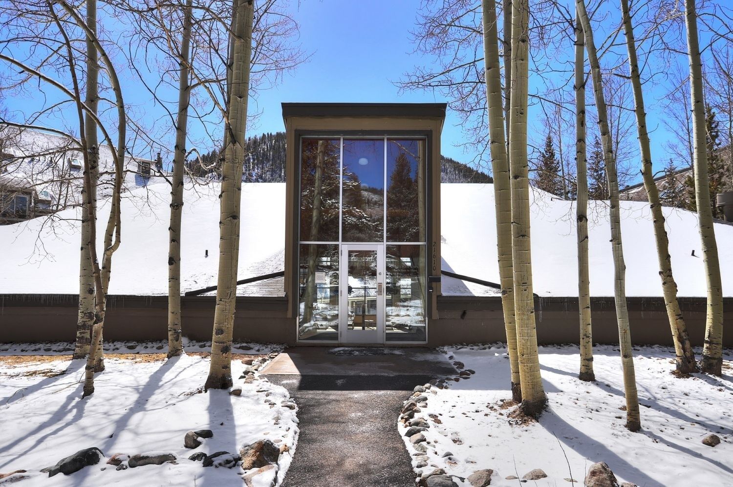 Un edificio con puerta y ventanas de vidrio, rodeado de árboles y nieve.