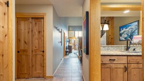 A hallway with wooden doors, a tiled floor, and a kitchen area with granite countertops and wooden cabinets. - 2056 The Pines 2 Bedroom Condo by RedAwning (Keystone)