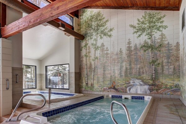 A spa area with a hot tub, wooden beams, and a forest mural on the wall.