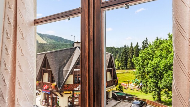 A view through a window of a building with a mountain backdrop, featuring a restaurant and a car parked outside. - Harrachov Lookout by Interhome (Harrachov)
