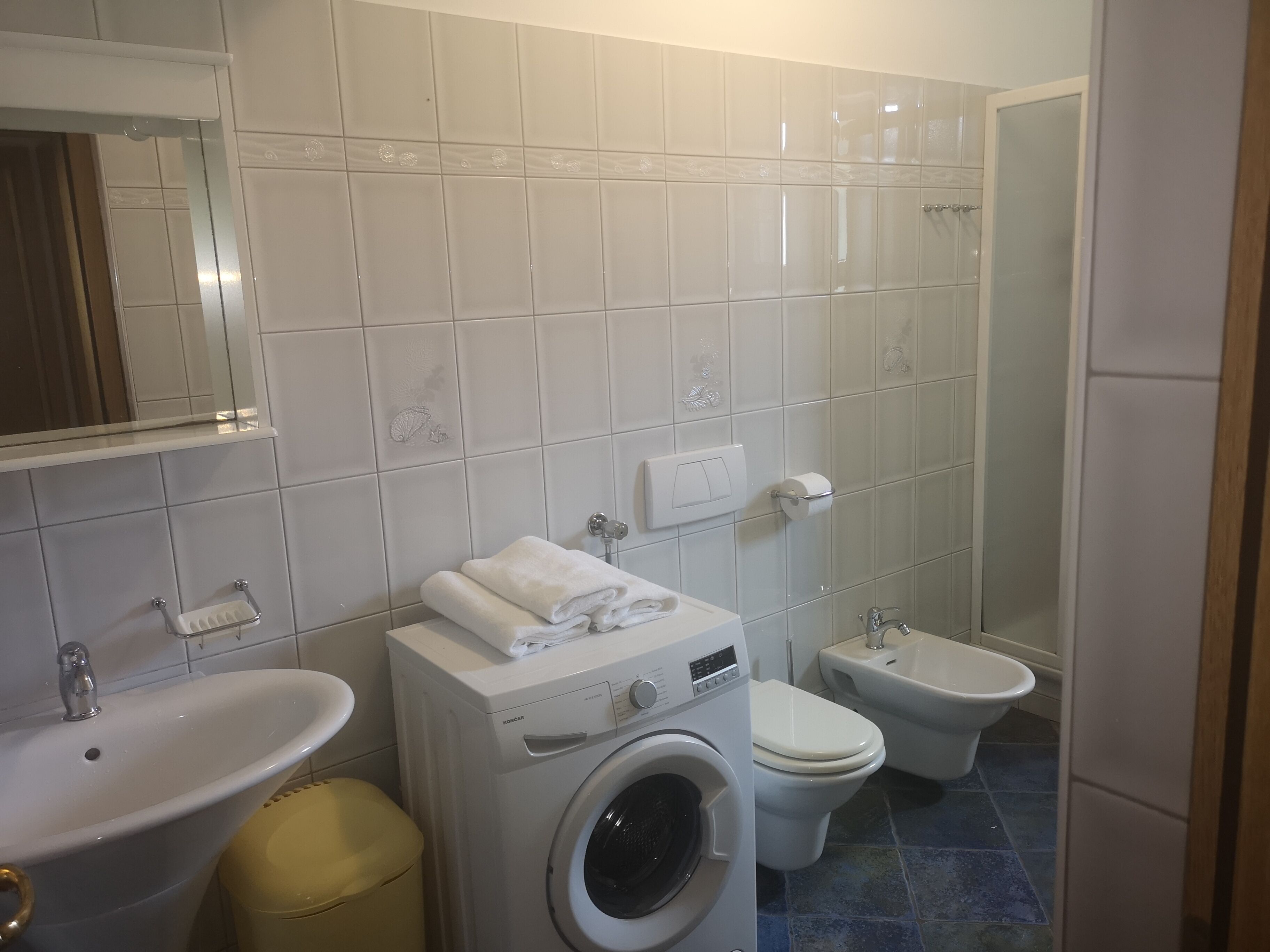 A bathroom with a sink, washing machine, toilet, bidet, and a mirror.