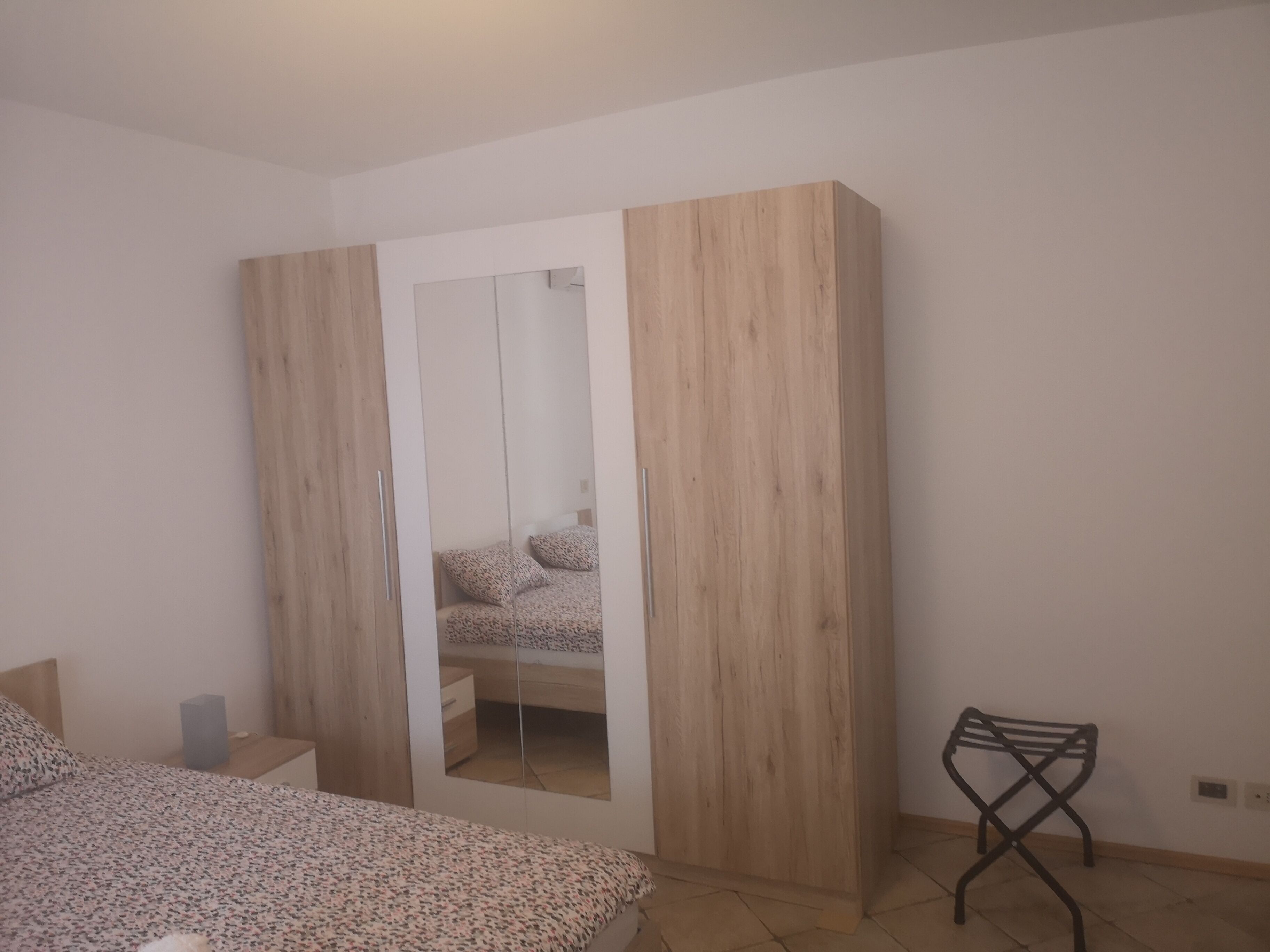 Un dormitorio con cama, armario, espejo y una mesita.