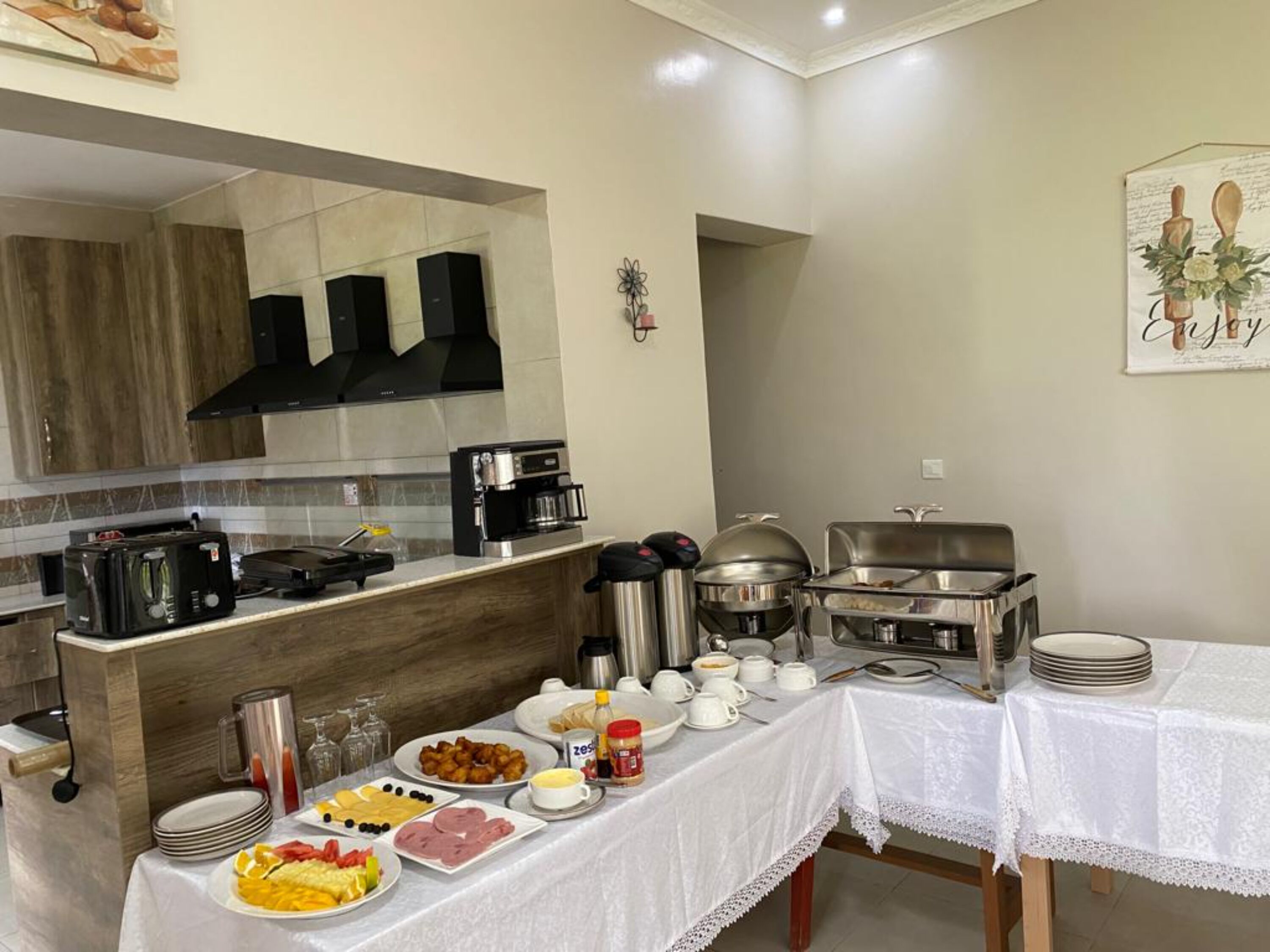 A breakfast buffet setup with various food items, a coffee machine, and a dining area with a table set for two.