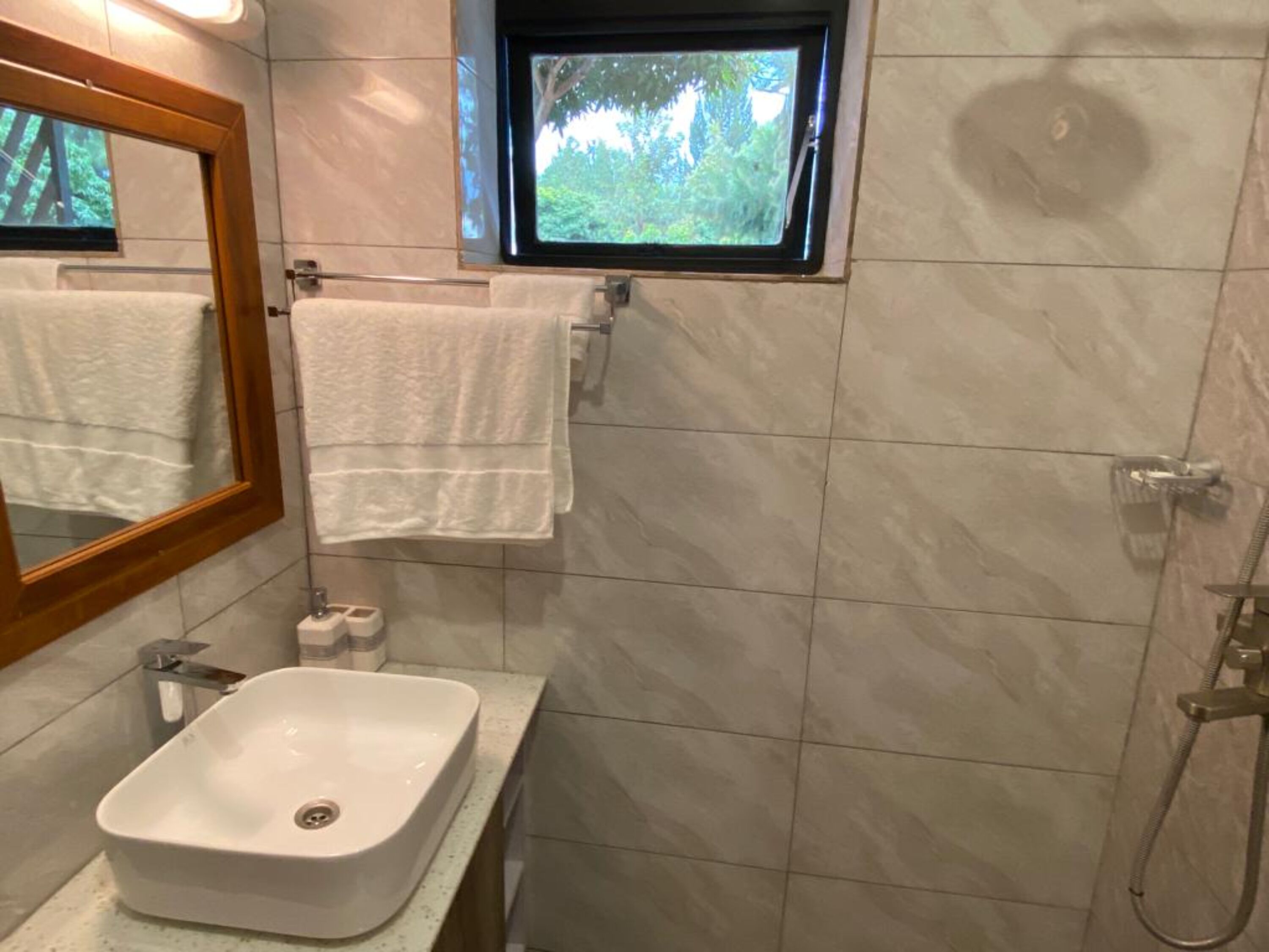 A bathroom with a white sink, a mirror, a window, and a shower.