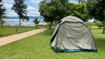 A tent set up on a grassy area with a lake and trees in the background.