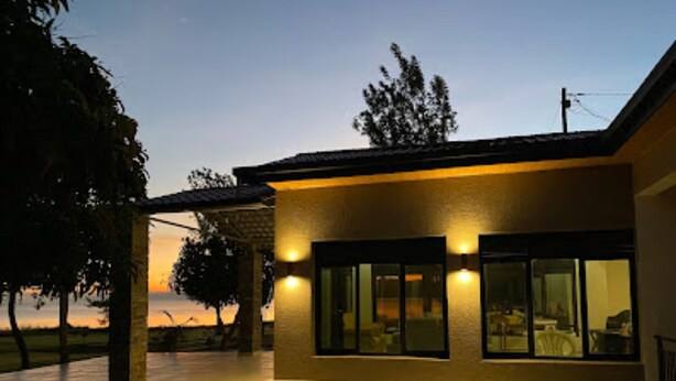 Una casa moderna con techo plano, ventanas amplias y un exterior bien iluminado al anochecer.