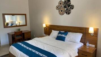 A hotel room with a bed, bedside tables, a mirror, and wall decor.