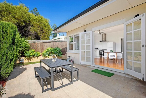 A patio with a table and chairs, a thatched roof structure, and a view into a kitchen area.
