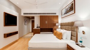 Una habitación de hotel moderna con una cama grande, una mesita de noche, un televisor montado en la pared y un ventilador de techo.