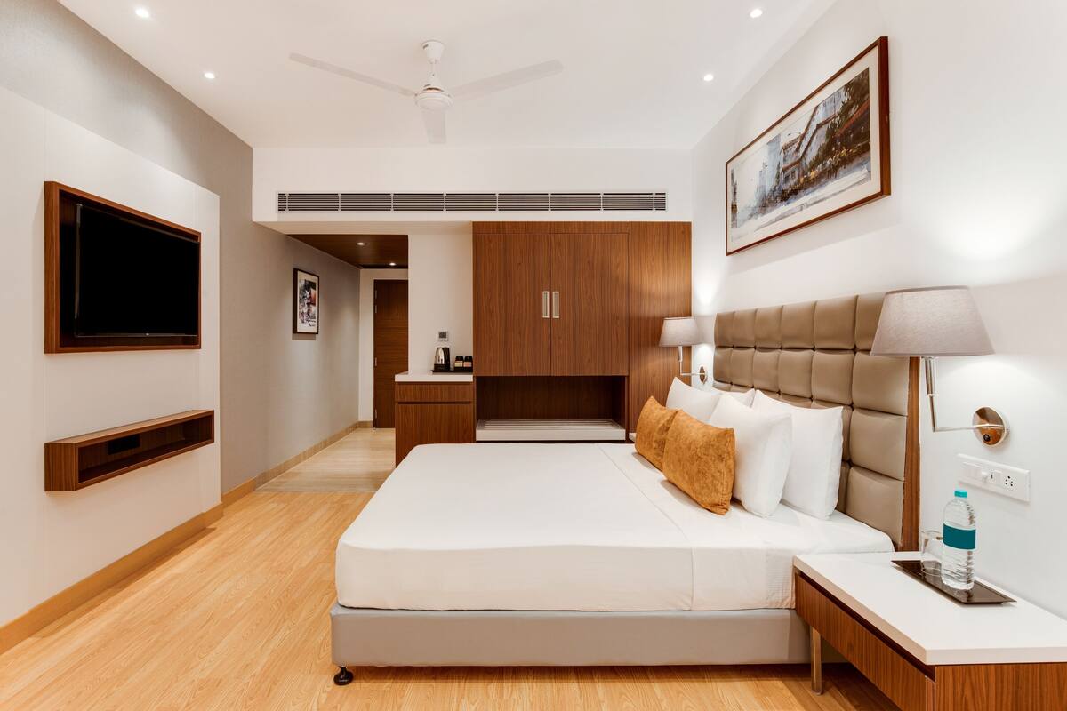 A modern hotel room with a large bed, a bedside table, a wall-mounted TV, and a ceiling fan.