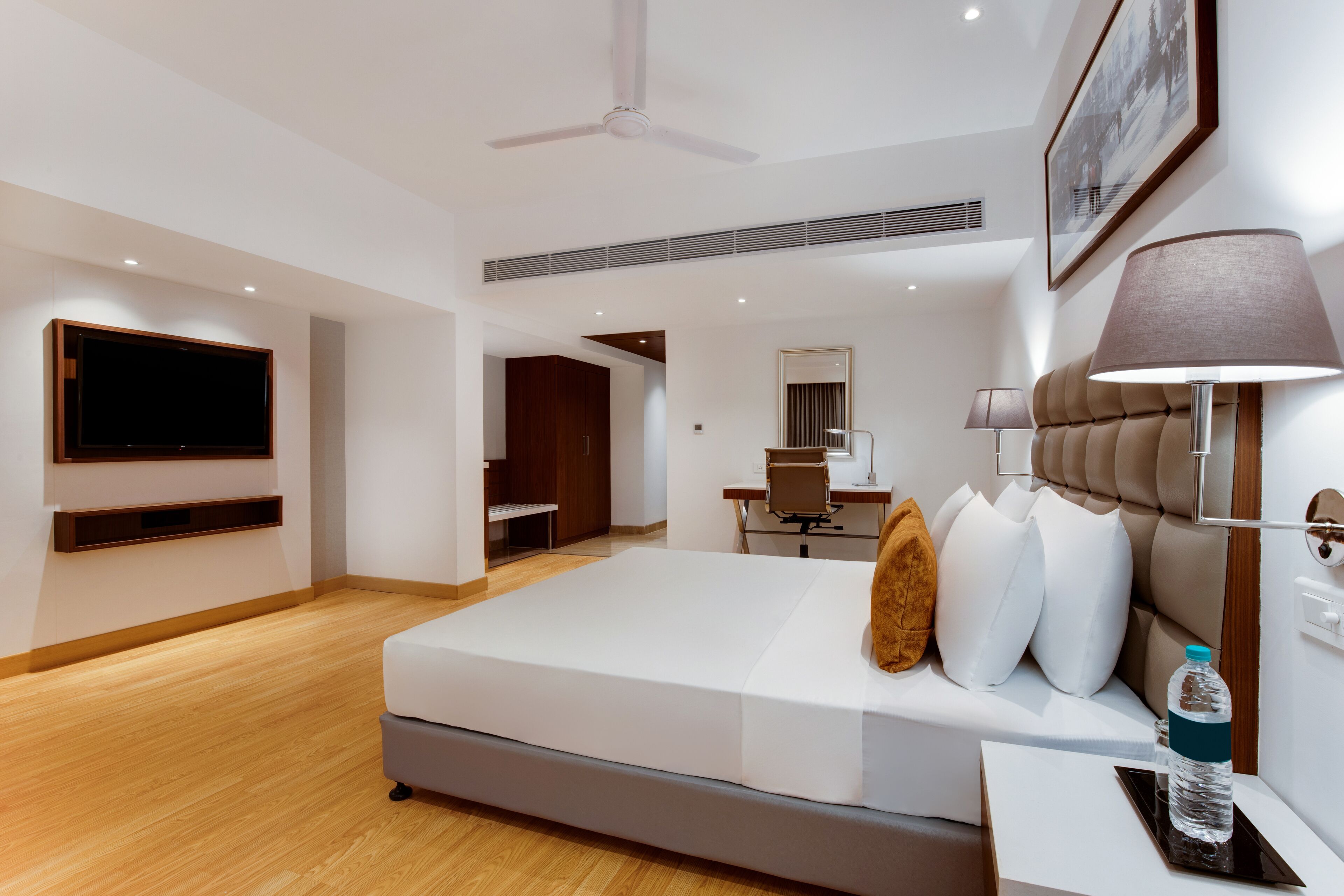 A modern hotel room with a large bed, a desk, a chair, a flat-screen TV, and a ceiling fan.