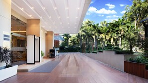 Un amplio pasillo interior con diseño moderno, que incluye una pared de vidrio con vistas a un exuberante jardín con palmeras y otra vegetación.