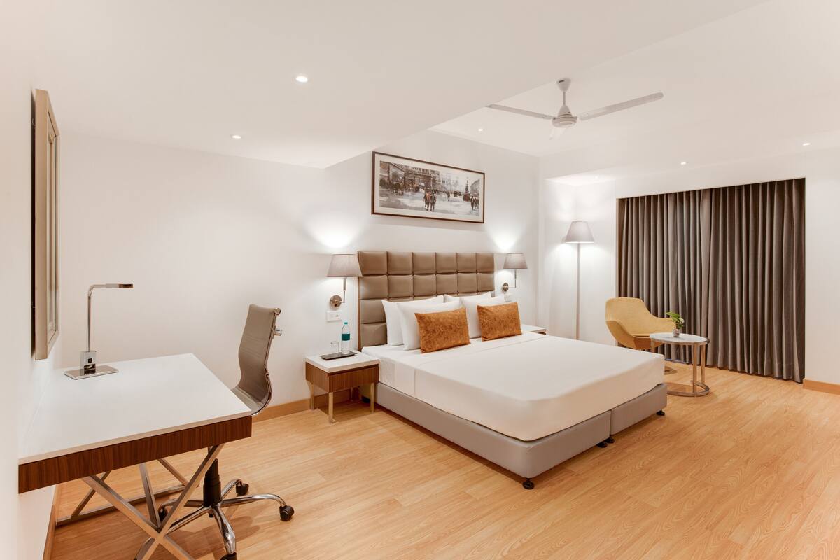 A modern hotel room with a large bed, a desk, a chair, a small table, and a ceiling fan.