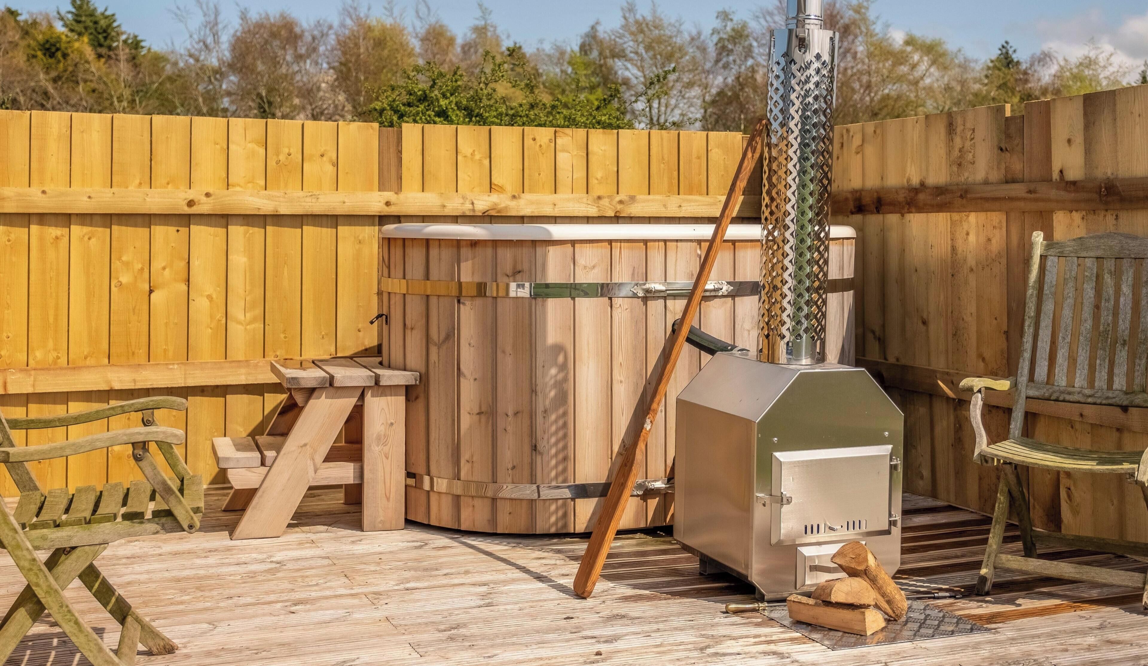 A wooden deck with a hot tub, a grill, and a wooden bench.