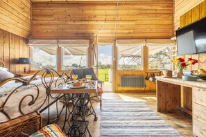 A cozy wooden cabin with a bed, dining table, and a TV. - The Cricket Pavilion, Warham, Norfolk (Warham)