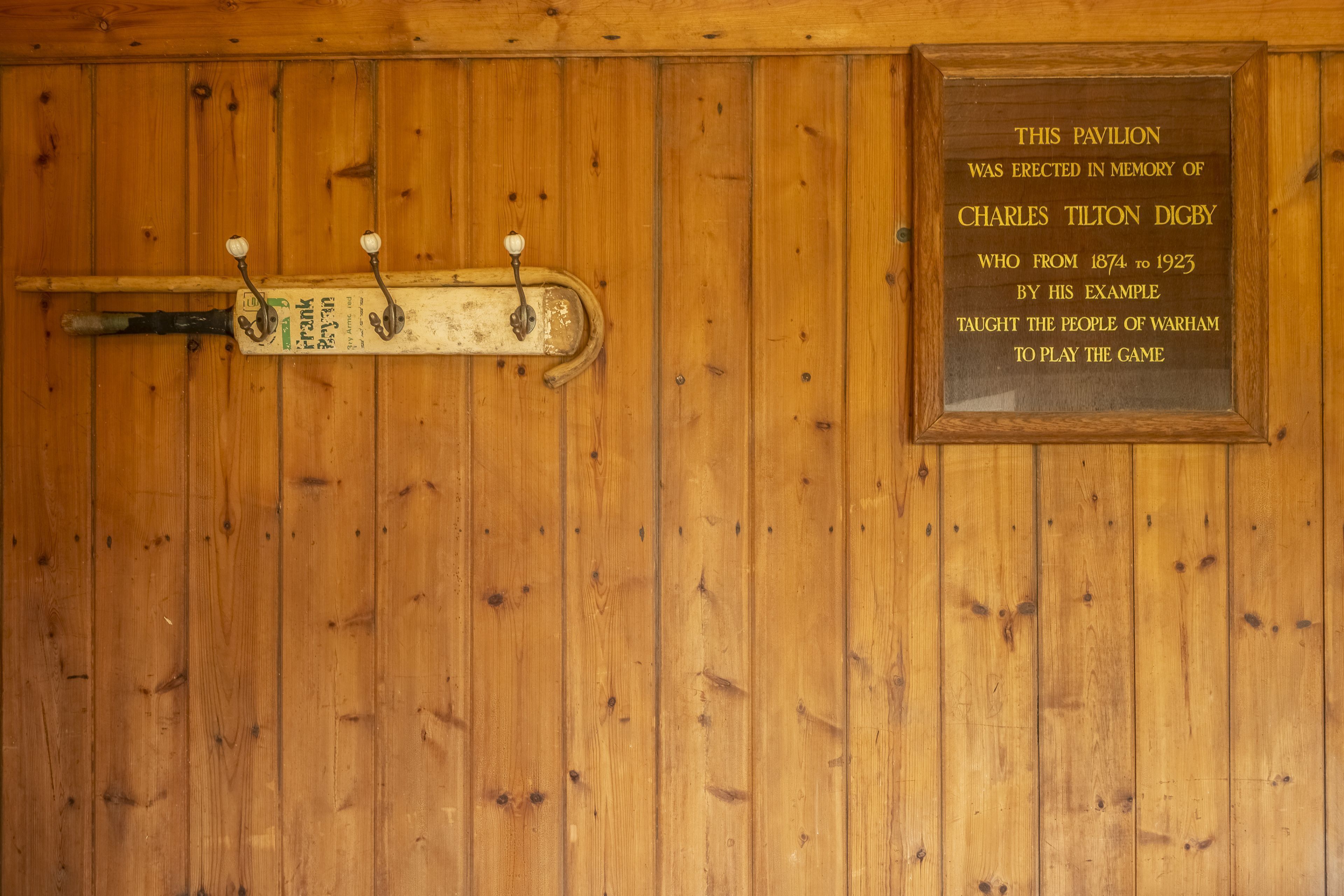 A wooden wall with a plaque commemorating Charles Tilton Digby and a wooden bat hanging on a rack.
