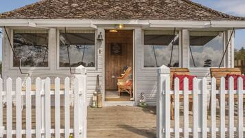 A small, white wooden building with a tiled roof, a wooden door, and a white picket fence.