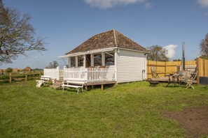 A small white house with a porch, surrounded by a wooden fence and a grassy yard. - The Cricket Pavilion, Warham, Norfolk (Warham)