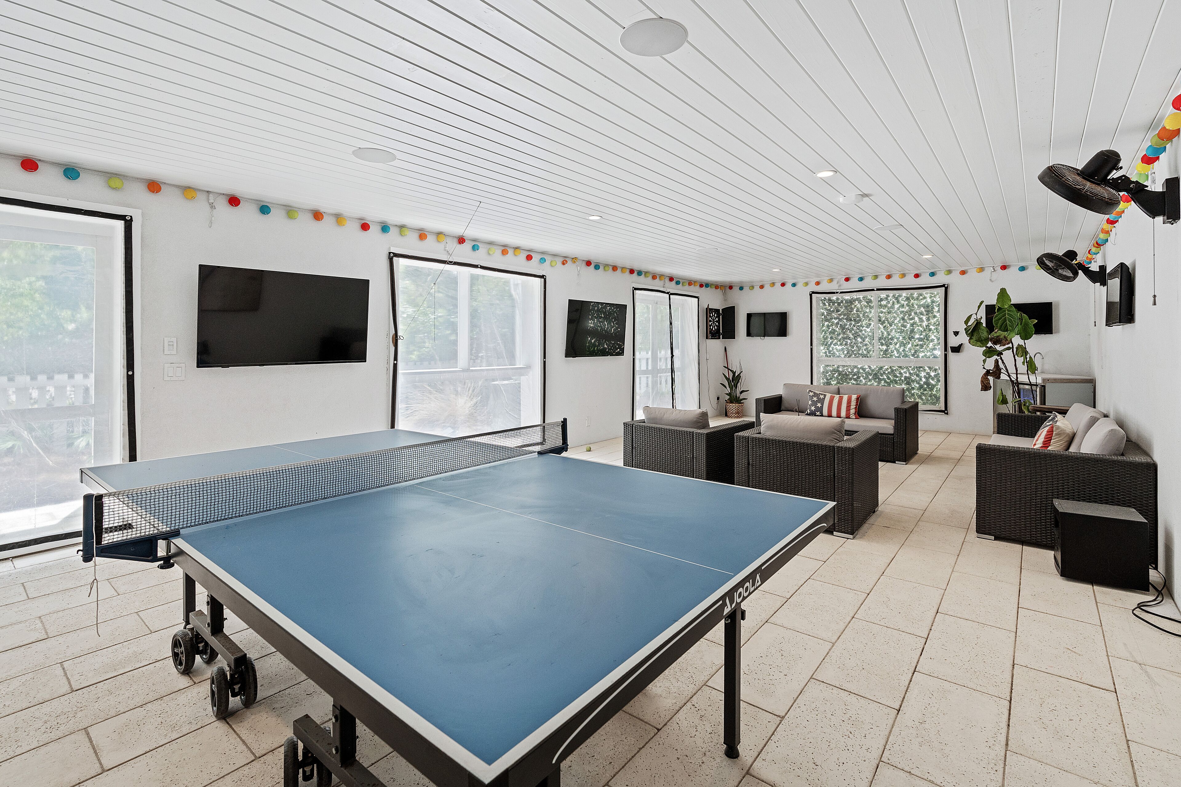 Una habitación amplia con mesa de ping pong, asientos cómodos y ventanas grandes.