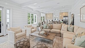 A spacious living room with a large sectional sofa, a coffee table, and a view of the kitchen in the background. - Royal Blue | Gated Neighborhood, Dedicated Beach Access, Golf Cart + Bikes (SANTA ROSA BEACH)