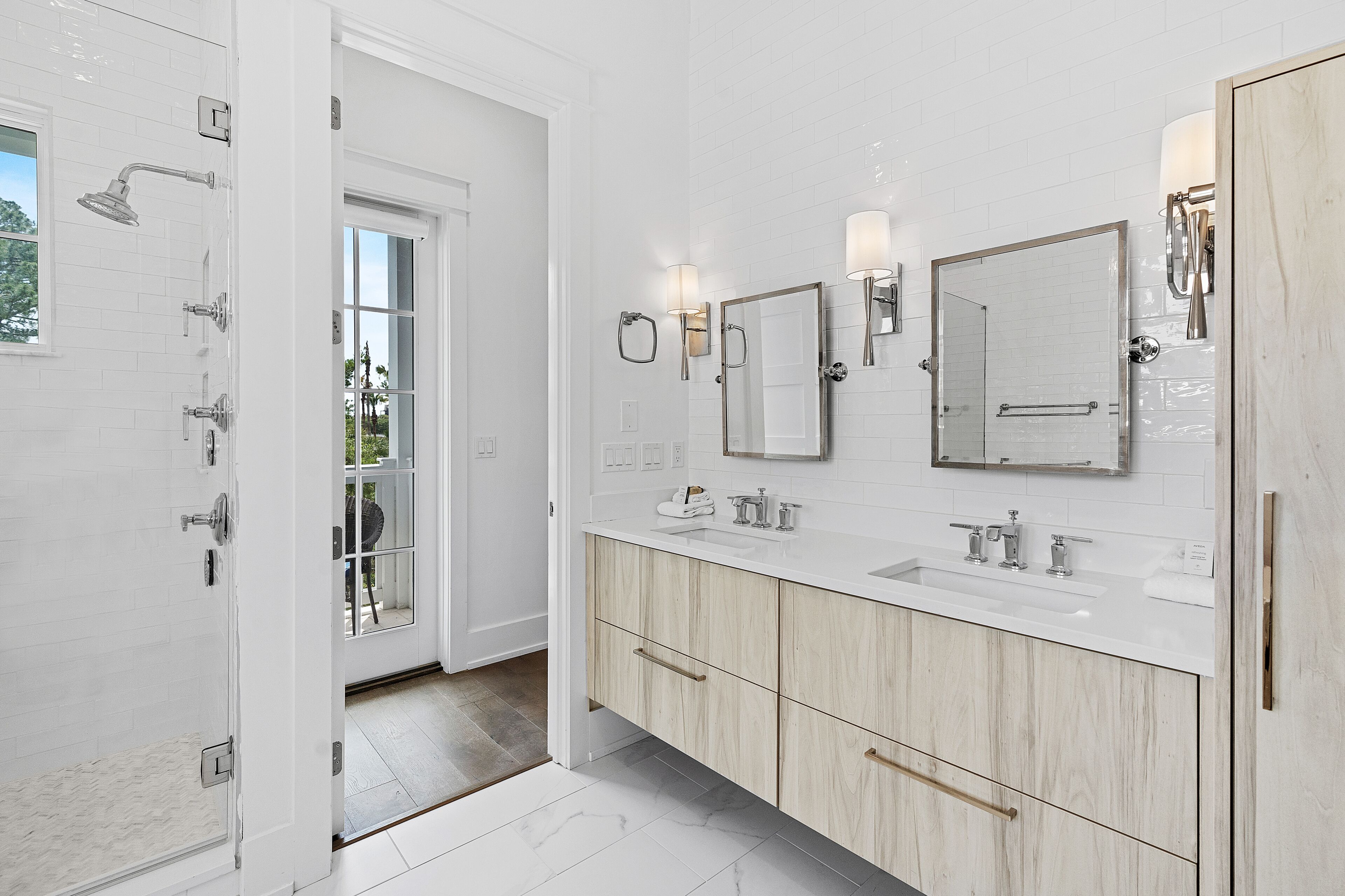 A modern bathroom with white subway tiles, a large mirror, two sinks, and a shower area.
