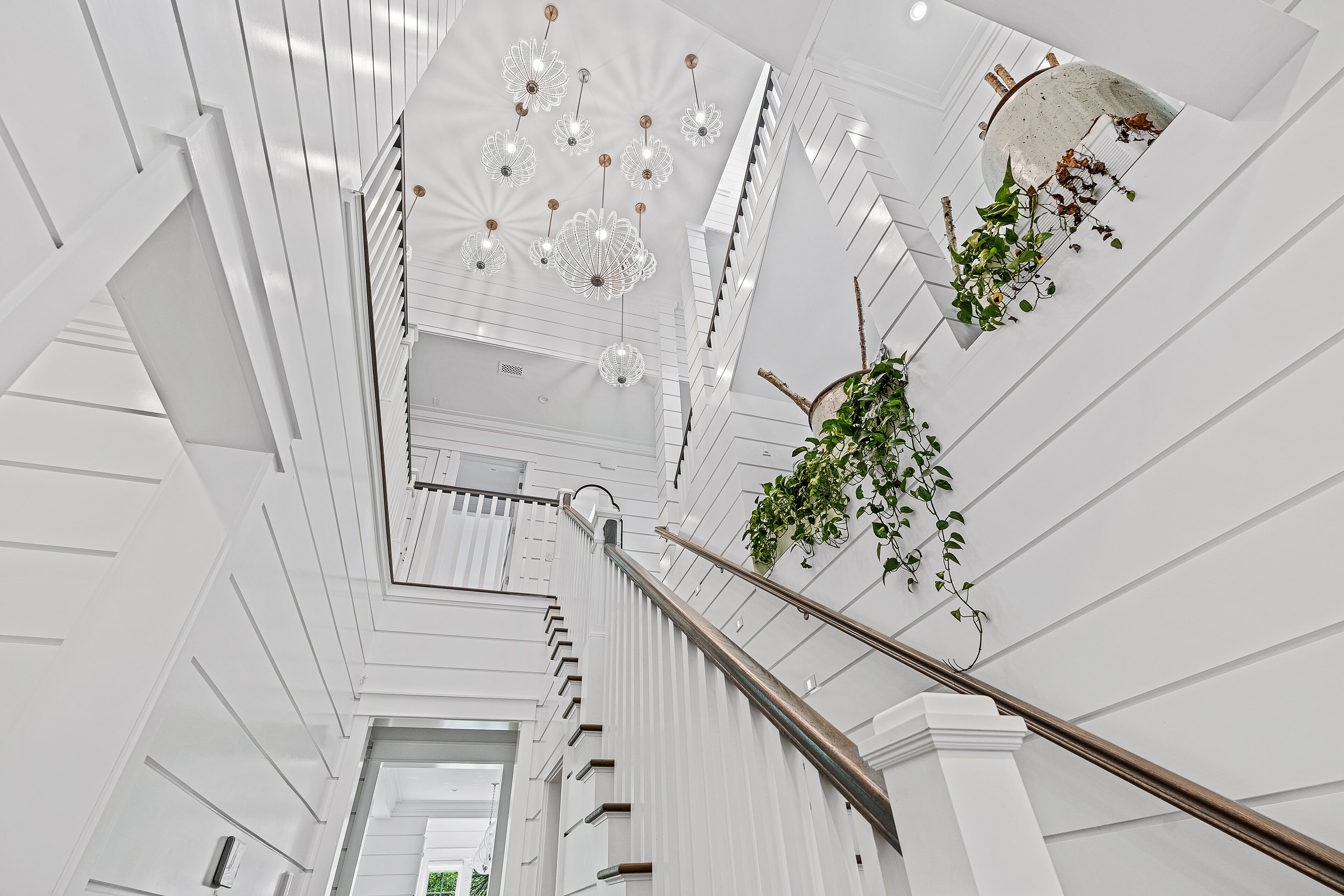 A modern interior with a staircase, white walls, and hanging plants.