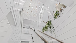 A modern interior with a staircase, white walls, and hanging plants. - Royal Blue | Gated Neighborhood, Dedicated Beach Access, Golf Cart + Bikes (SANTA ROSA BEACH)